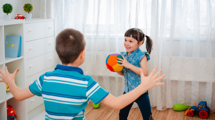 native children a boy and a girl play in a children's game room, throwing a ball. The concept of interaction of todlers, communication, mutual play, quarantine, self-isolation at home