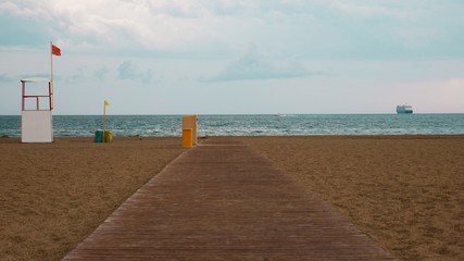Abandoned beach with wooden planks due to the storm. With a red flag warning of danger. In the background, a cruise ship is receding.