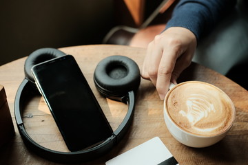 woman hand holding hot coffee latte cup,with smartphone,headphone and credit card on wooden table.