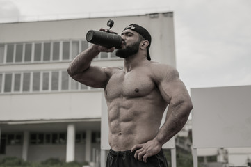 young strong athlete male drinking water from black bottle during outdoor fitness workout on...