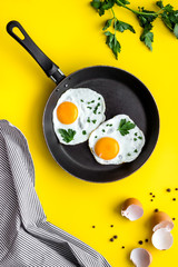Fried eggs on frying pan on yellow desk top-down