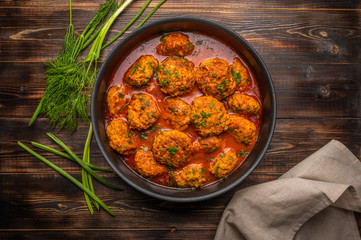 Homemade meatballs in tomato sauce in a pan on a dark wooden background. Nearby linen napkin, green onions and dill