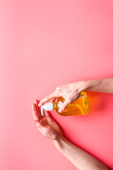 Dispensing sanitizer on hands - coronavirus prevention - pink background top-down copy space