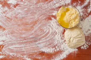 Grated cheese with an egg in a plate and sprinkled flour with stocked dough on a wooden table while cooking, top view