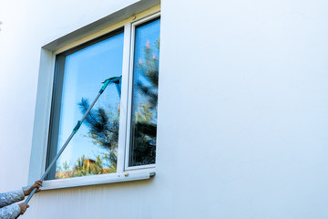 Hand washing windows with a squeegee. The window reflects the sky and the silhouette of spruce