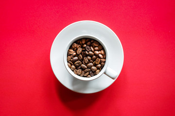 Flat lay of roasted coffee beans in white coffee cup with red background 