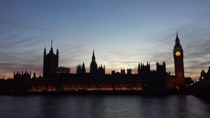 Fototapeta na wymiar Illuminated Palace Of Westminster By Thames River At Sunset
