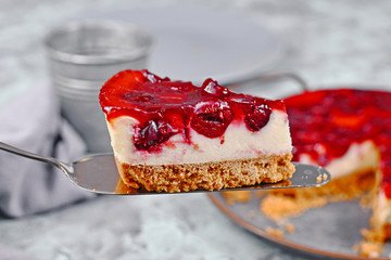 Slice of cheesecake glazed with cherry fruit topping on cake server