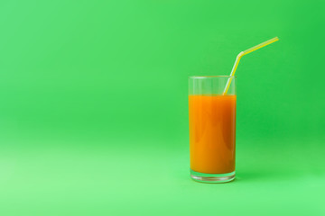 carrot juice in a glass with a straw on a green background