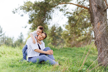 Fototapeta premium Happy young mother is playing with her baby in a park on a green lawn. Happiness and harmony of family life. Great family vacation. Good weekend. Mothers Day. Holiday. The concept of a happy family