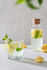 Refreshing lemonade with lemon, mint, ginger and ice in glass and bottle on white concrete background. Summer refreshing drink. Cold detox water with lemon. Copy space. Menu