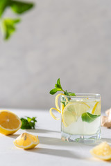Cold detox water with lemon. Glass with lemonade or mojito cocktail with lemon, ginger and mint, cold refreshing drink with ice on white background. Menu, recipe. Copy space