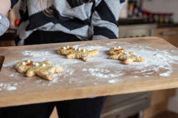 Woman hands holding baking tray with homemade gingerbread man cookies in the kitchen