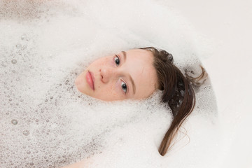 Baby girl face in bathtub among soap suds and bubbles. Child bathing