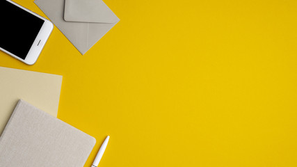 Flat lay, top view office table desk. Workspace with blank notebook, smartphone, envelope, pen on yellow background. Minimal style modern workplace