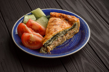 Horizontal image, Flat-lay, of vegetable pie with spinach and salmon on blue plate from above on a textured black background.