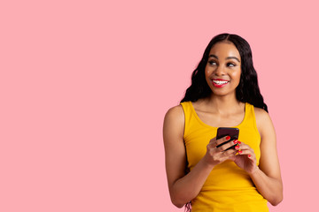 Portrait of a happy young woman with black hair using smart phone, smiling and looking up at copy...
