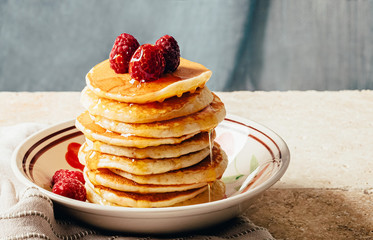 Pancakes poured with honey decorated with raspberries on a plate on a blue background. Copy space
