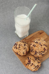 Fresh organic homemade cookies with chocolate chips and dried berries on wooden board with glass of milk on table