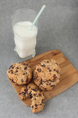 Fresh organic homemade cookies with chocolate chips and dried berries on wooden board with glass of milk on table