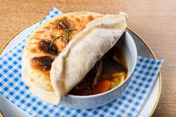 Fish stew in a white bowl, served with a pita bread cover on top. Levantine East Mediterranean food
