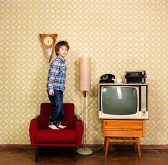 Vintage art portrait of liitle boy jumping on armchair in room with interior from 70s 20th century,...