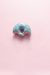 close-up view of bitten donut with bubblegum flavor with frosted and filled with fruit jam and cream, colored glazed and sprinkled donuts on pink background
