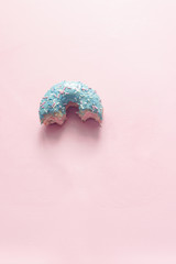 close-up view of bitten donut with bubblegum flavor of blue color with frosted and filled with fruit jam and cream, colored glazed and sprinkled donuts on pink background