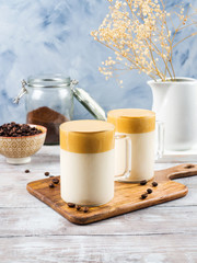 Whipped dalgona coffee drink in glass mug on wooden board. Cozy breakfast with trendy beverage
