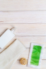 Green waxing strips with mint and cooling effect, body moisturizer and white cotton towel on wooden background with copy space. Flat lay.