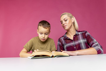 Mother helps her son with homework, while are they together reading a book.