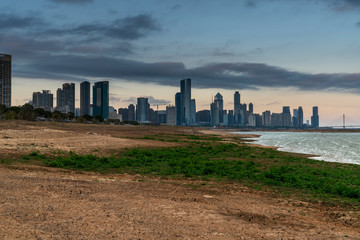 Tall skyscrapers of a modern, metropolitan cityscape tower over a beautiful, white, sandy beach on a warm, sunny day.