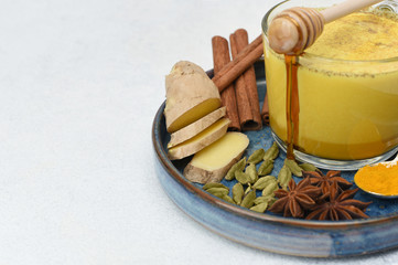 Golden Milk, made with turmeric and other spices. A glass cup with golden milk and ingredients around on light background with copy space. Turmeric, cinnamon, ginger, honey, star anise, cardamom.