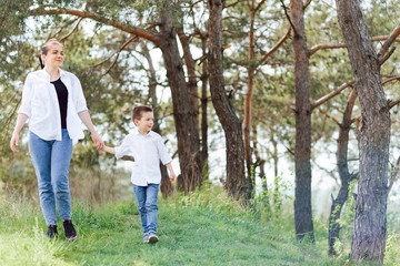 Naklejka na ściany i meble Mother and little son happy family. Attractive mom,kid boy are walking carefree outdoors summer. Parent woman goes on nature together with child,summer,spring day.Light,copy space. Happy family.