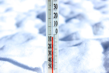 A glass thermometer for measuring the temperature in the center sticks out of the snow with a value of minus 3 degrees Celsius. White background.