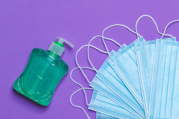 Medical protective disposable face mask to cover nose and mouth with a bottle of hand sanitiser isolated against a purple background. Healthcare Coronavirus quarantine, hygiene concept.