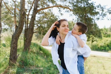 Fototapeta premium Happy young mother is playing with her baby in a park on a green lawn. Happiness and harmony of family life. Great family vacation. Good weekend. Mothers Day. Holiday. The concept of a happy family