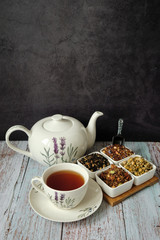 Mug with red tea, teapot and dry tea leaves. Dark background with copyspace