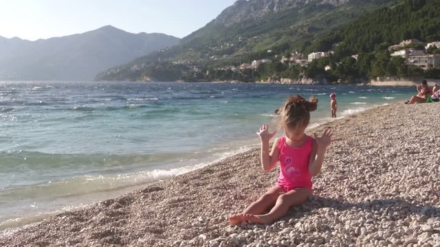 little girl sitting on the beach, playing, windy day. Punta Rata Beach in Brela, Croatia, Adriatic