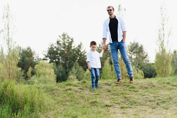 Handsome dad with his little cute son are having fun and playing on green grassy lawn. Happy family concept. Beauty nature scene with family outdoor lifestyle. family resting together. Fathers day