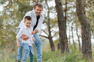 Happy father and son sitting in the park. Smiling young man spending time together with his son.