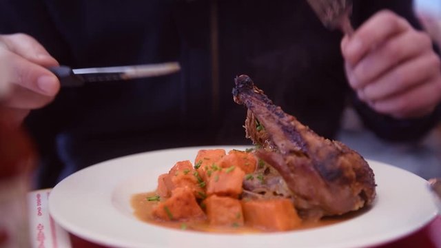 Une personne mange une cuisse de canard dans une brasserie