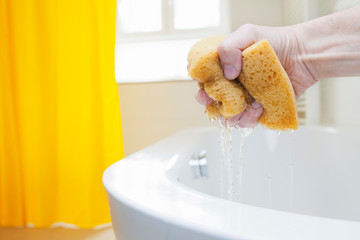Hand squeezing a sponge with water in a bright bathroom