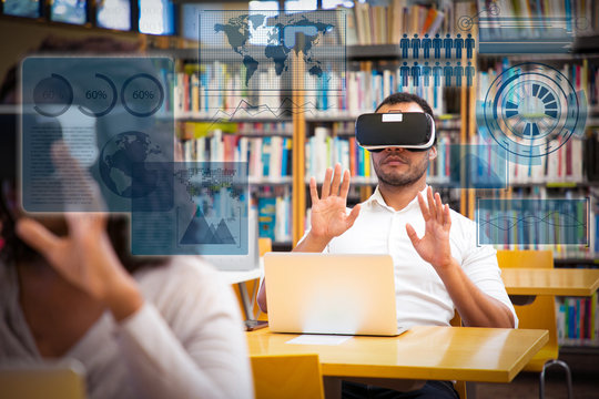 Multiethnic group of students using VR gadgets for studying. Man and woman in virtual reality headsets sitting at desks with laptops and touching virtual global map charts. VR simulators concept - Powered by Adobe