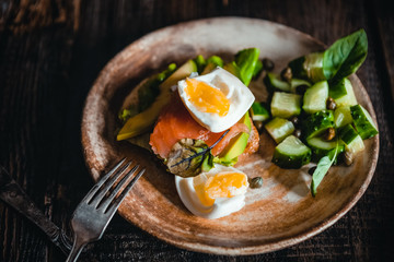 poached egg with vegetables, avocado, salmon and herbs in bowls on brown wooden table, healthy breakfast concept