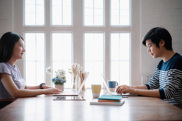Young asian couple discussing together and typing on computer during working day in home office. Working from home concept