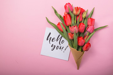 red  beautiful tulips in an ice cream waffle cone with card Hello you on a color background. Conceptual idea of a flower gift. Spring mood