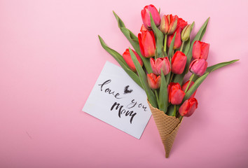 red  beautiful tulips in an ice cream waffle cone with card Love you mom  on a color background. Conceptual idea of a flower gift. Spring mood