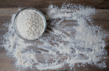 Glass bowl of white flour on wooden table, top view.