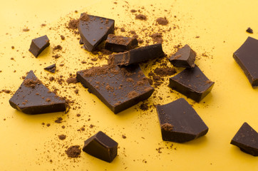 Closeup of pieces of dark chocolate and cocoa powder on the yellow background